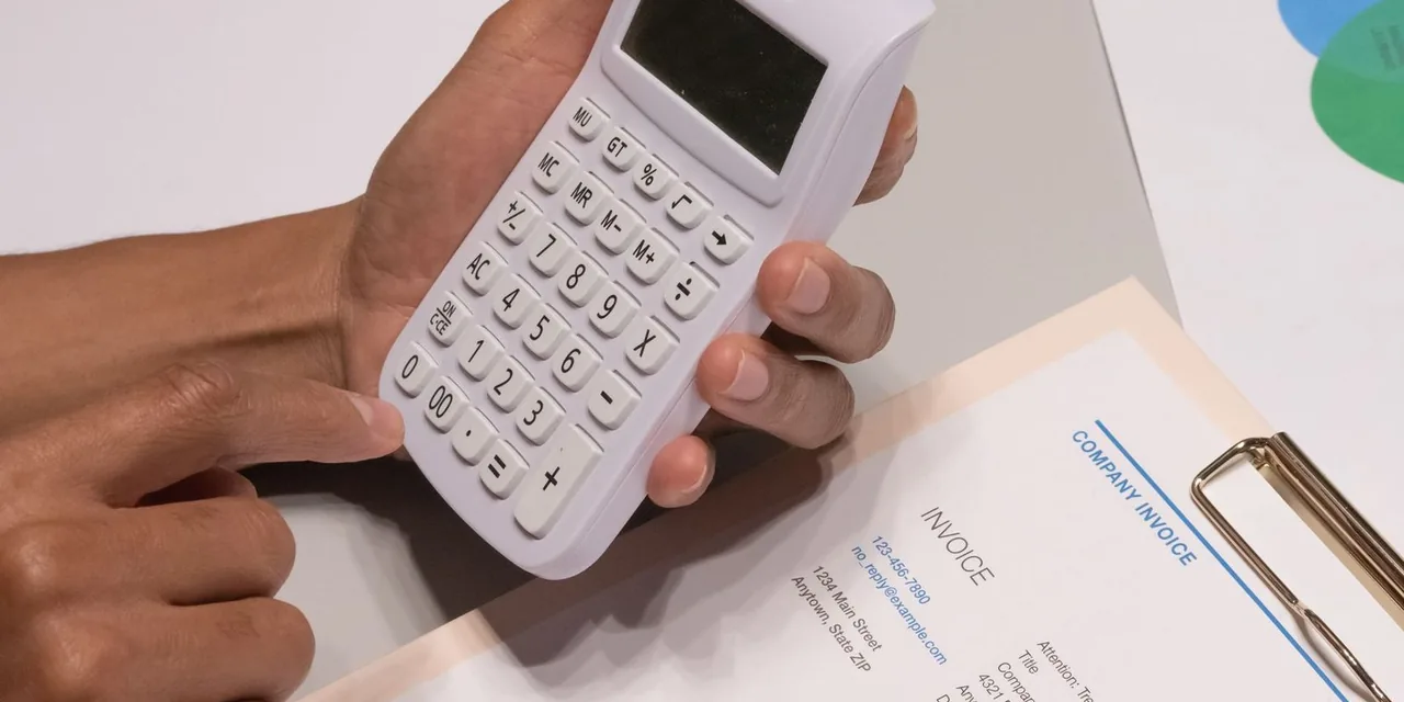 Close-up of hands using a calculator next to a company invoice, depicting a financial calculation concept.
