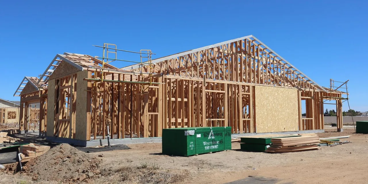Wooden house frame construction under clear blue sky, sunny day.